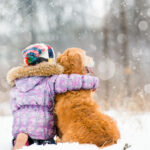 Little girl sitting outside and hugging her dog in the snow