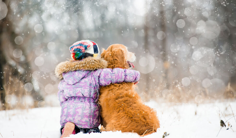 Little girl sitting outside and hugging her dog in the snow